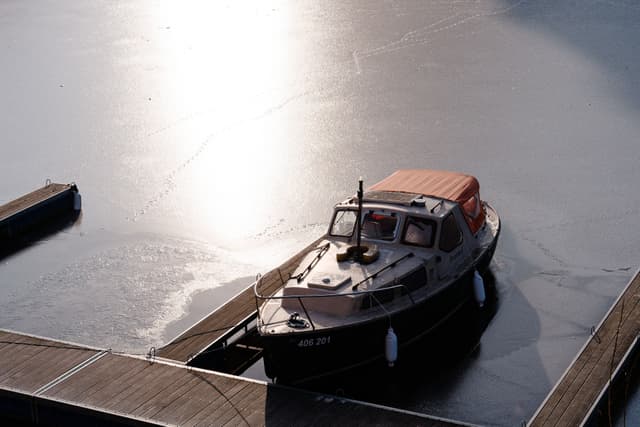 A boat docked at a pier on a calm, reflective body of water with sunlight glistening on the surface