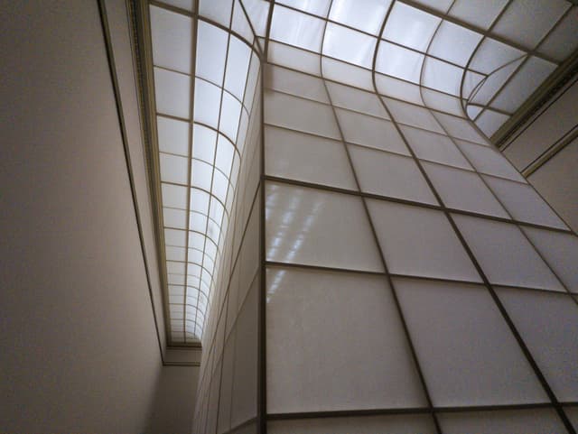 A modern architectural interior with large, translucent panels and a curved, grid-like ceiling allowing natural light to filter through