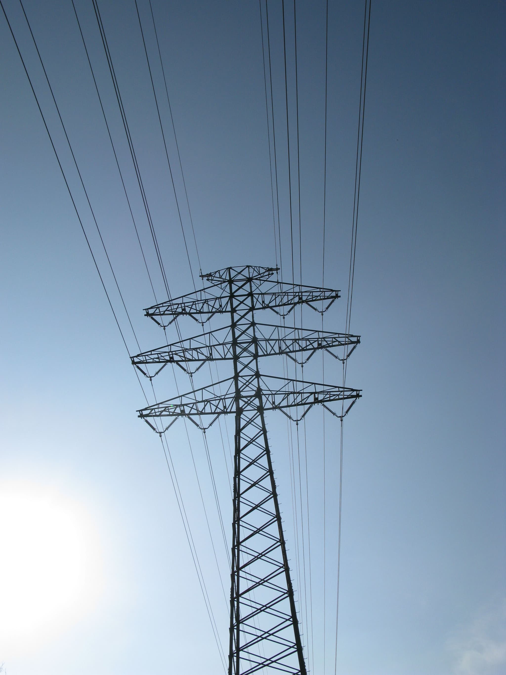 A tall electricity transmission tower with multiple power lines against a clear blue sky