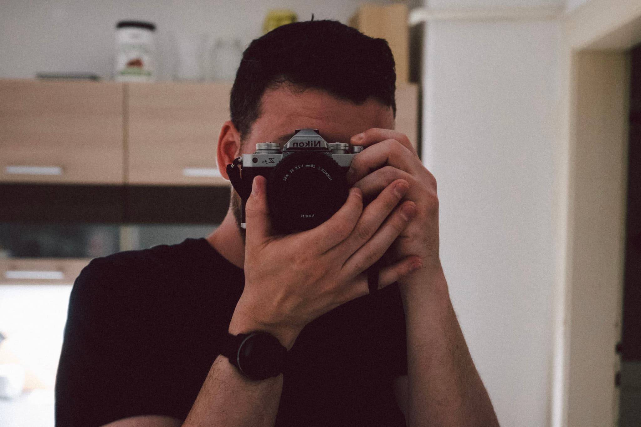 A person holding a camera up to their face, taking a photo in a room with wooden cabinets in the background