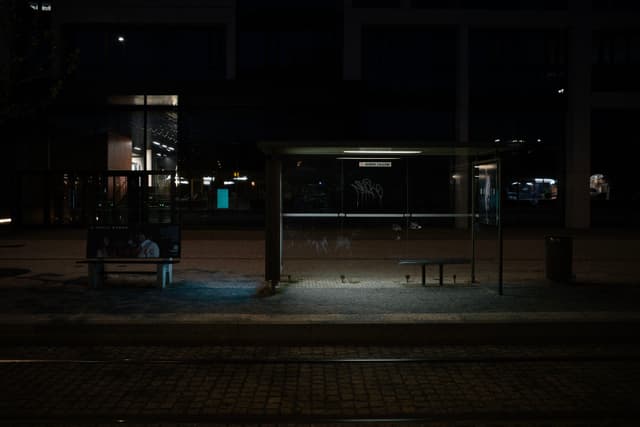 A dimly lit bus stop at night with empty benches and a person sitting on the left side