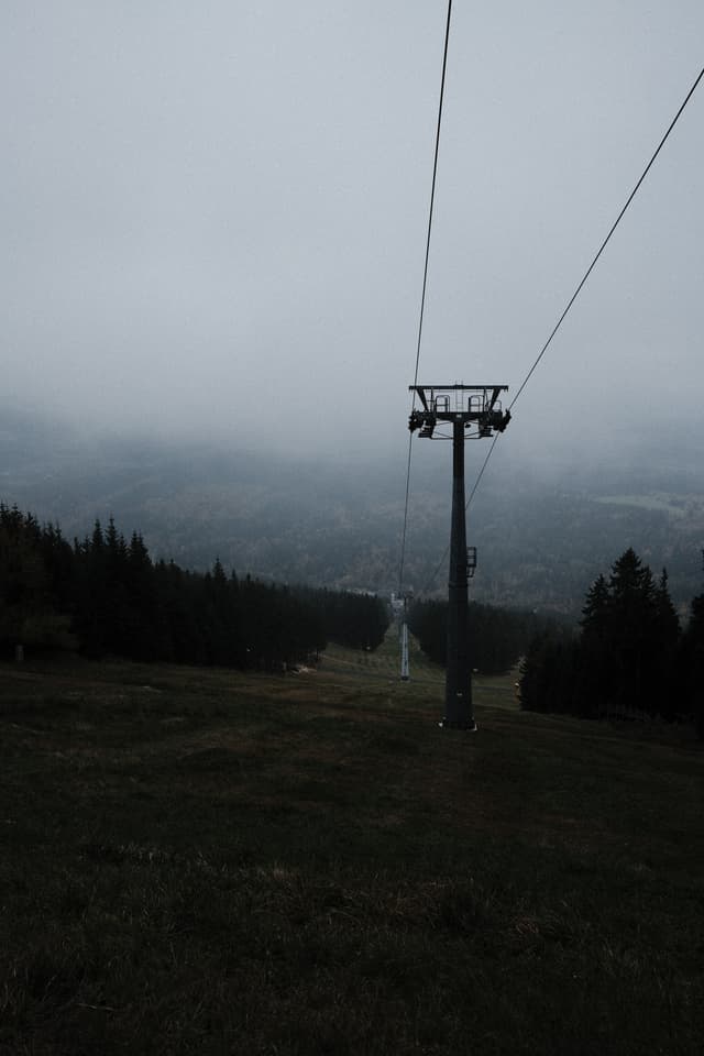 Foggy landscape with a single ski lift sliding down a hillside amidst evergreen trees