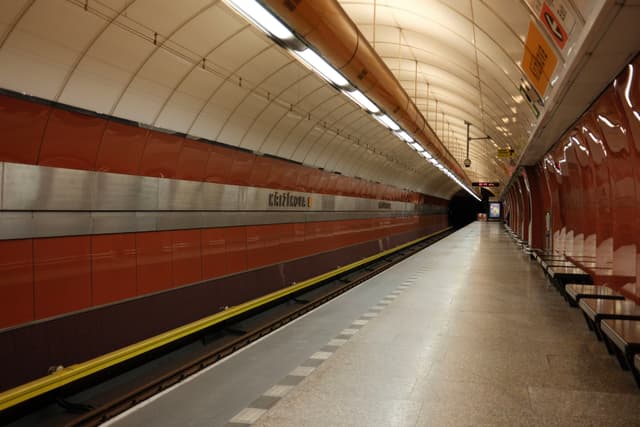 An empty underground train station platform with a curved ceiling and red-brown walls