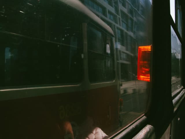 A view from inside a vehicle, looking out at a red bus and city buildings, with reflections on the window