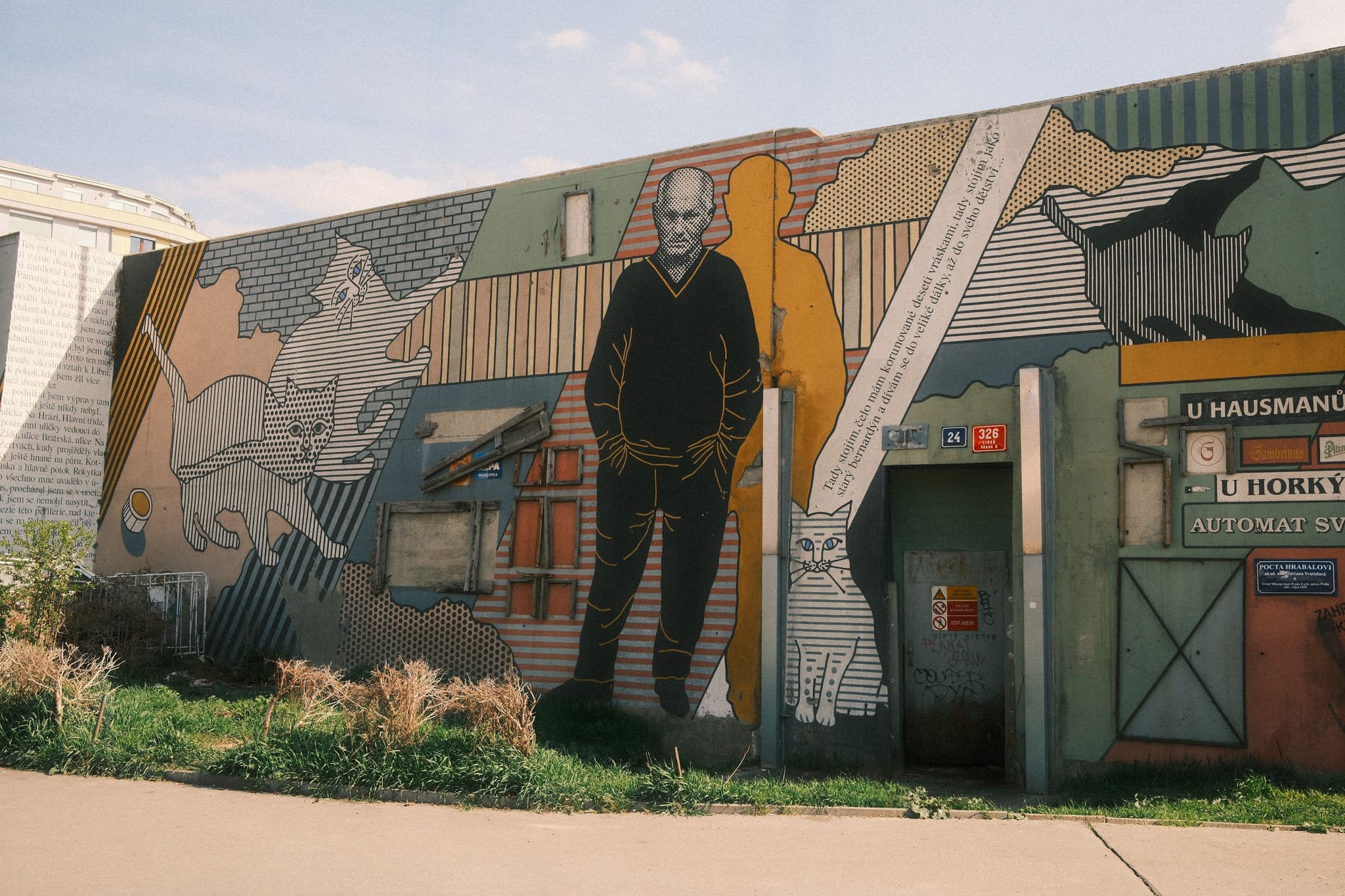 A mural on a building wall featuring a person in a hooded jacket, surrounded by various animals, including cats and birds, with a mix of geometric patterns and vibrant colors