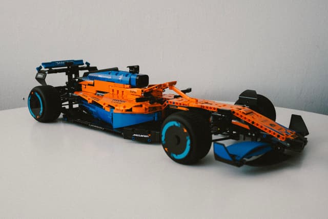 A detailed LEGO model of a Formula 1 race car in orange and blue colors, displayed on a white surface