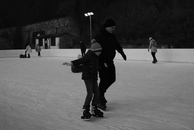 A black and white photo of people ice skating on an outdoor rink, with a child and an adult in the foreground