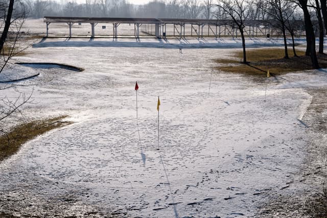 A snow-covered golf course with visible flags and trees in the background