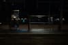 A dimly lit bus stop at night with empty benches and a person sitting on the left side