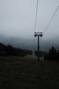 Foggy landscape with a single ski lift sliding down a hillside amidst evergreen trees