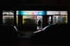 A dimly lit street scene with a person entering a brightly illuminated store, flanked by parked cars