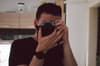 A person holding a camera up to their face, taking a photo in a room with wooden cabinets in the background